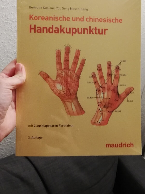 Hand hält Buch Koreanische und chinesische Handakupunktur von Kubiena und Mosch-Kang 